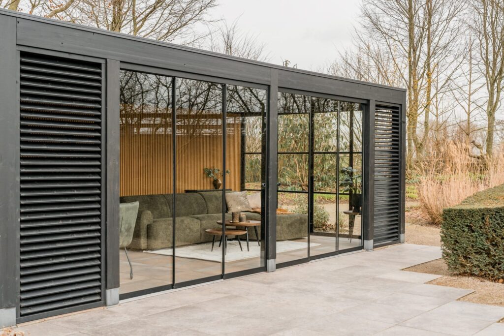 Stijlvolle zwarte houten veranda met glazen wanden en moderne loungehoek in een natuurlijke tuinomgeving"